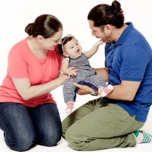 A mother and father hold up a baby girl between themselves