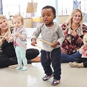 Two blond moms, their girls, and a little black boy bang sticks together with the music